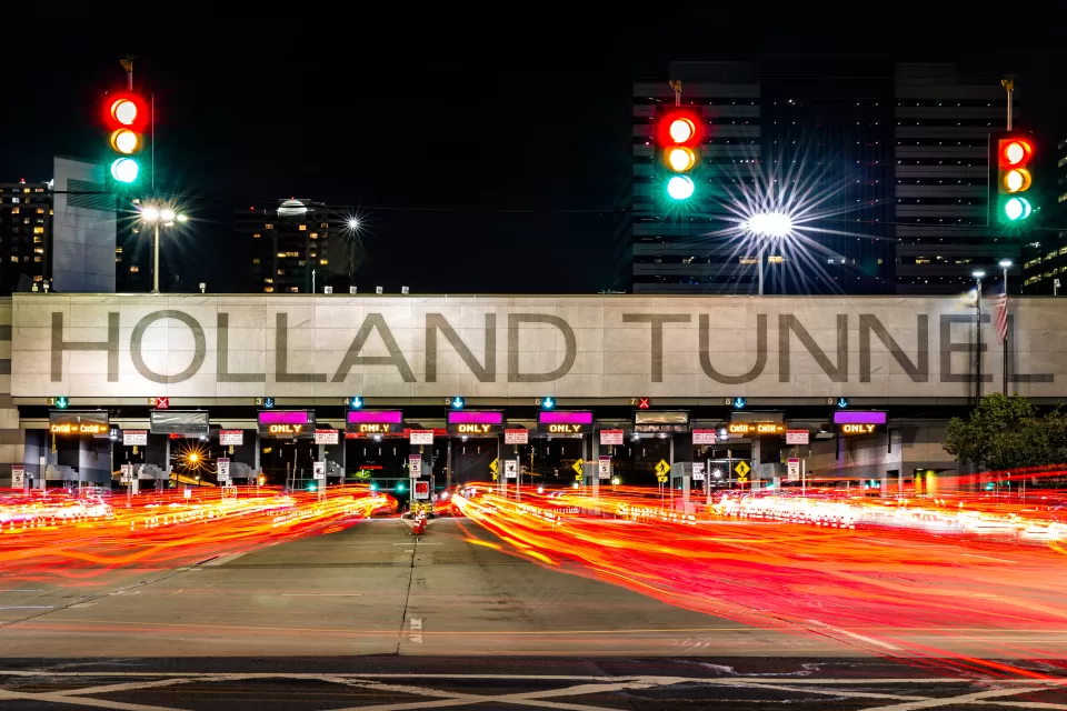 View of large HOLLAND TUNNEL sign tollbooths with blurred red taillights in foreground